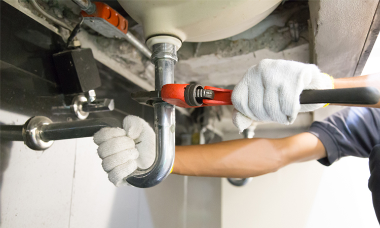 Plumber fixing white sink pipe with adjustable wrench.